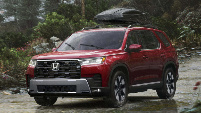 Вид спереди в 3/4 на Honda Pilot, едущего по мелкому ручью в лесистой местности