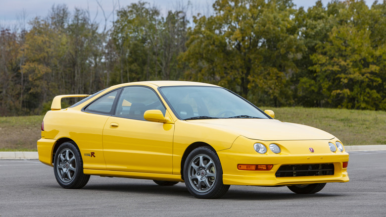 Желтая Acura Integra Type R 2001 года выпуска, припаркованная перед лесом на стоянке, вид спереди справа в 3/4