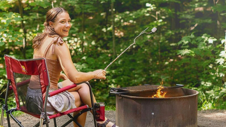 Женщина сидит на рокере GCI Outdoor Freestyle Rocker и жарит зефир на костре.