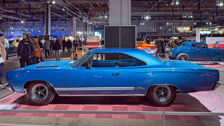 Вид сбоку на синий Plymouth GTX, припаркованный на крытом автосалоне.