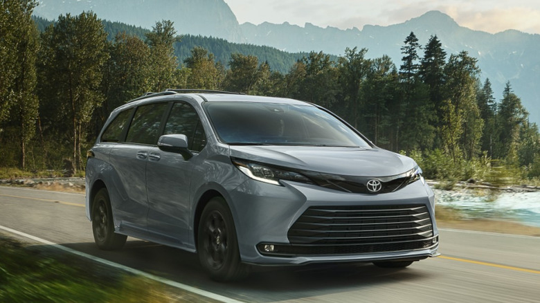 Вид спереди на 3/4 гибридного минивэна Toyota Sienna Woodland в горной местности, проезжающего мимо ручья