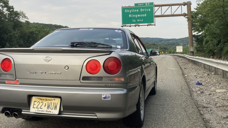 Nissan Skyline R34 2000 года выпуска, припаркованный на обочине шоссе со знаком выхода, 