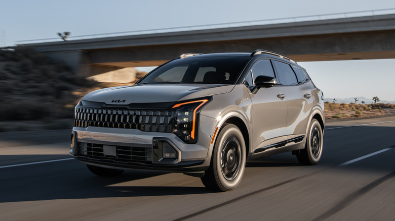 Светло-коричневый Kia Sportage едет по дороге под эстакадой