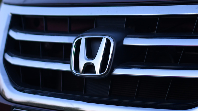 Крупный план серебряного логотипа Honda на передней части автомобиля.