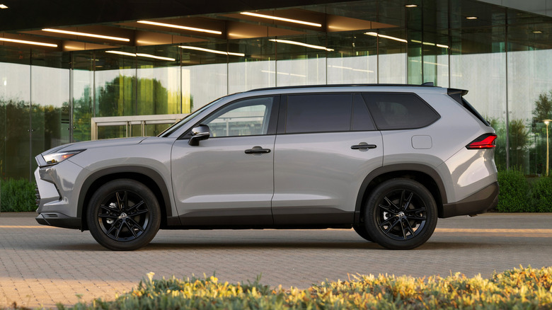 Серая Toyota Grand Highlander 2026 года выпуска, припаркованная перед современным офисным зданием.