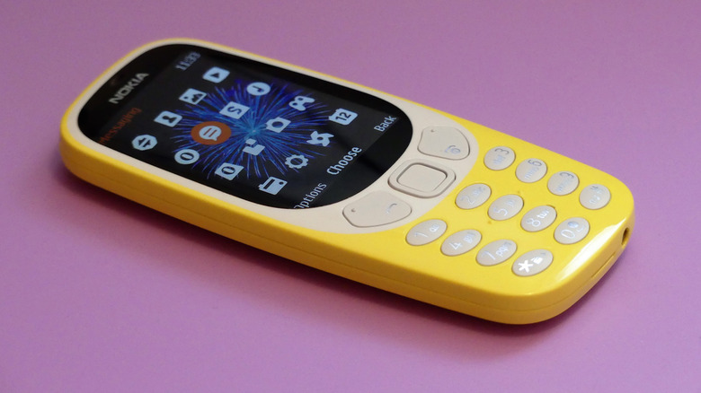 Функциональный телефон Nokia 3310 крупным планом на розовом фоне.