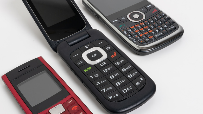 Мобильные телефоны 1990-х годов, в том числе раскладушка и Blackberry, на белом фоне.