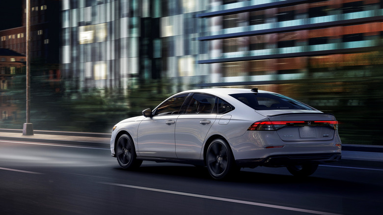 Вид сзади в 3/4 на белую Honda Accord, едущую по городу.