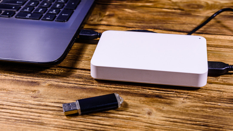 Ноутбук с подключенным к нему SSD и флэш-накопителем USB рядом с ним, все это на деревянном столе.