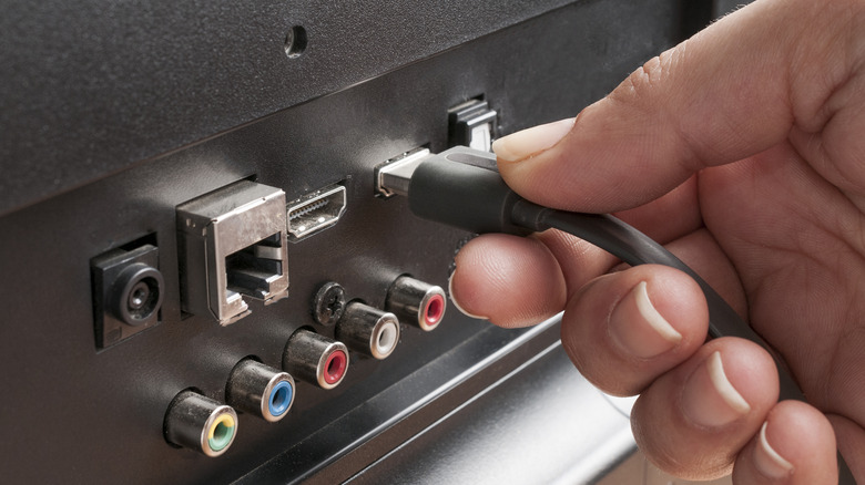 Человек, подключающий кабель HDMI к задней панели телевизора