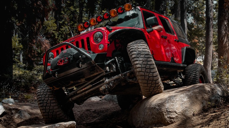 Красный Jeep Wrangler преодолевает труднопроходимую дорогу.
