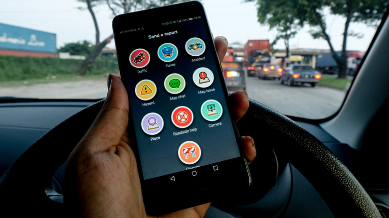человек держит смартфон и показывает экран отправки отчета в Waze внутри автомобиля