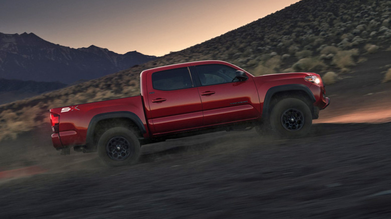 Вид сбоку на красный пикап Toyota Tacoma на пустынной тропе вечером.