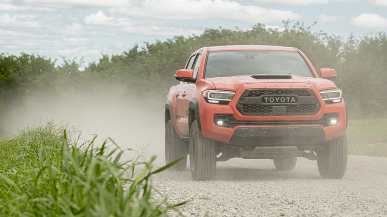 Вид спереди оранжевой Toyota Tacoma 2023 года выпуска на грунтовой дороге.