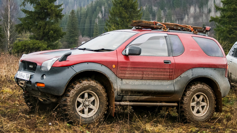 Грязный красный Isuzu VehiCross, припаркованный в поле.