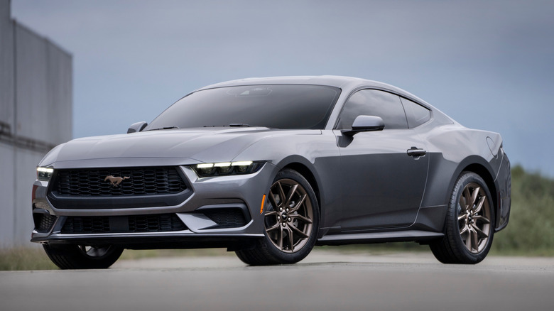 Ford Mustang EcoBoost 2026 года выпуска серого цвета, припаркованный возле промышленного здания.