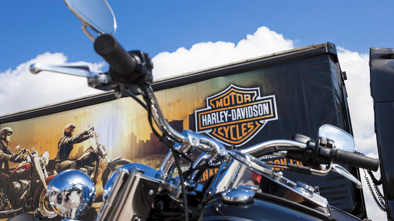 Крупный план руля крейсерского мотоцикла на фоне грузовика Harley-Davison.