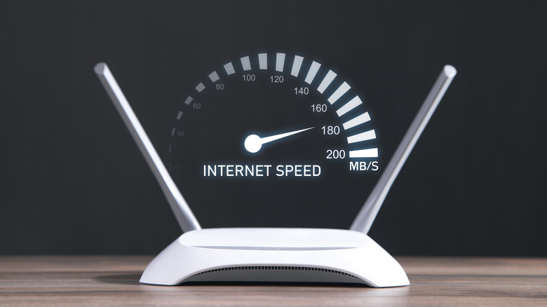 Маршрутизатор Wi-Fi с двумя антеннами, расположенный на деревянном столе, над которым расположен спидометр, показывающий скорость интернета.