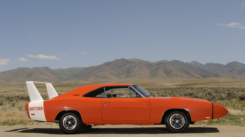 Оранжевый гоночный автомобиль Dodge Charger Daytona Nascar 1969 года выпуска, стоящий на грунтовой поверхности, с носовым обтекателем и белым крылом.