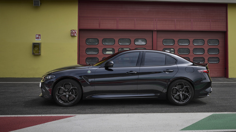 Вид сбоку на черный Alfa Romeo Giulia Quadrifoglio, припаркованный на гоночной трассе.