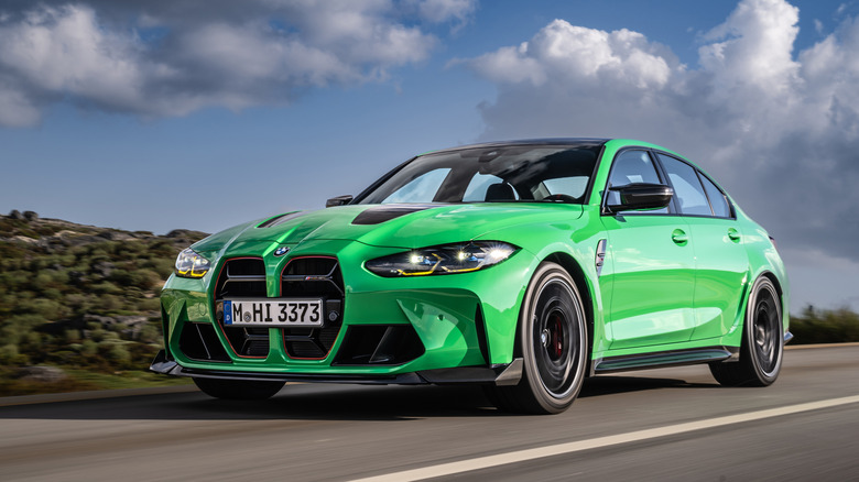 Вид спереди на 3/4 зеленого BMW M3 CS, едущего по проселочной дороге.