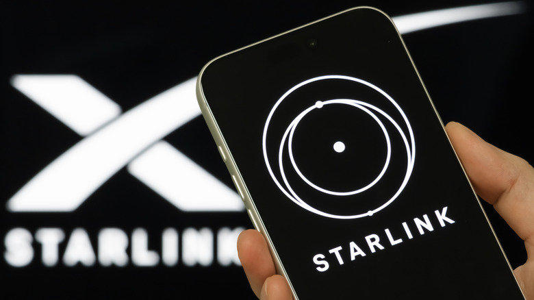 Рука держит сотовый телефон с белым логотипом Starlink на черном фоне.