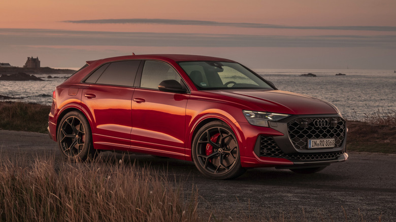 Совершенно новый Audi RS Q8 2027 года, припаркованный на берегу моря во время заката, вид спереди на 3/4