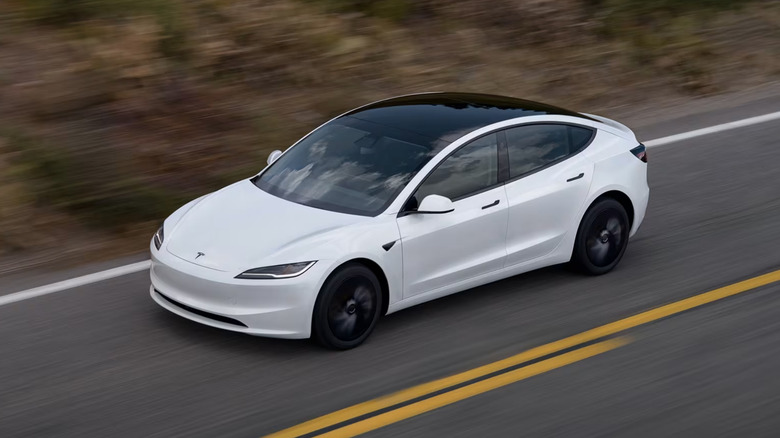 Tesla Model 3 едет по дороге, вид спереди 3/4, белый кузов, высокий угол