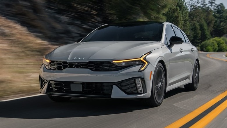 светло-серый Kia K5 2026 года едет по извилистой дороге