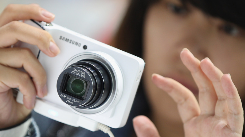 Женщина держит белую цифровую камеру Samsung.