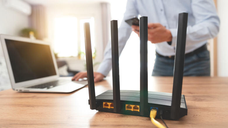 Маршрутизатор Wi-Fi на столе, а человек на заднем плане его настраивает.