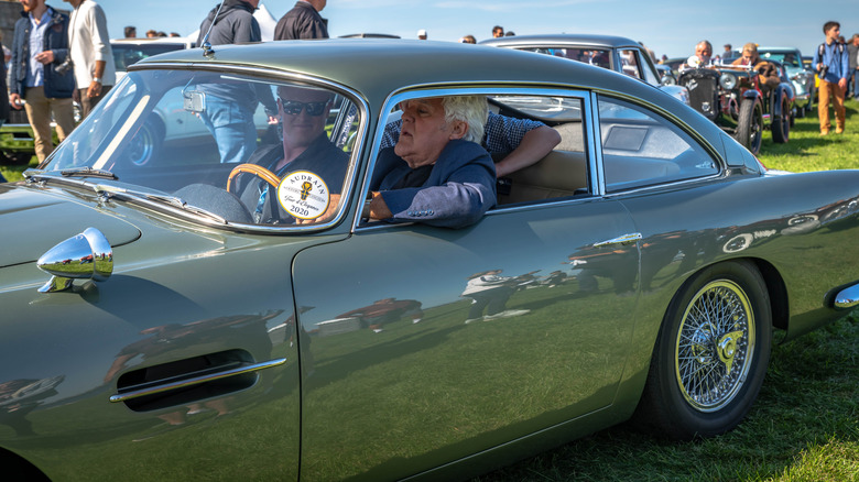 Джей Лено сидит в Aston Martin на мероприятии Audrain Concours.