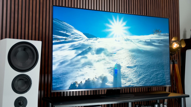 Телевизор Hisense U8QG, показывающий сцену заснеженных гор, рядом с ним белый динамик домашнего кинотеатра.