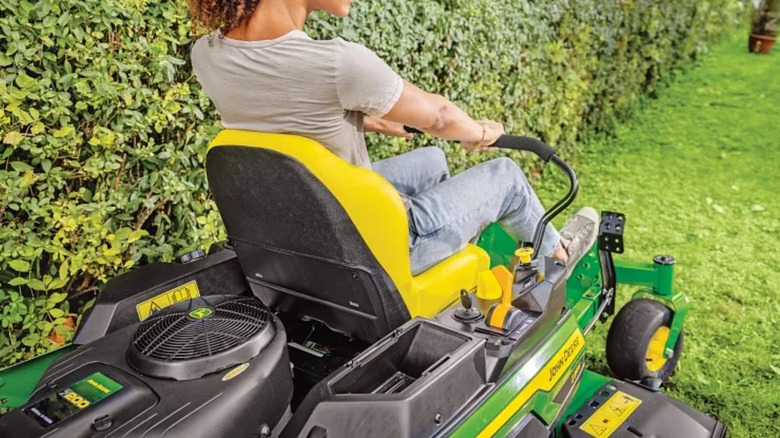 Женщина косит газон газонокосилкой John Deere с нулевым поворотом