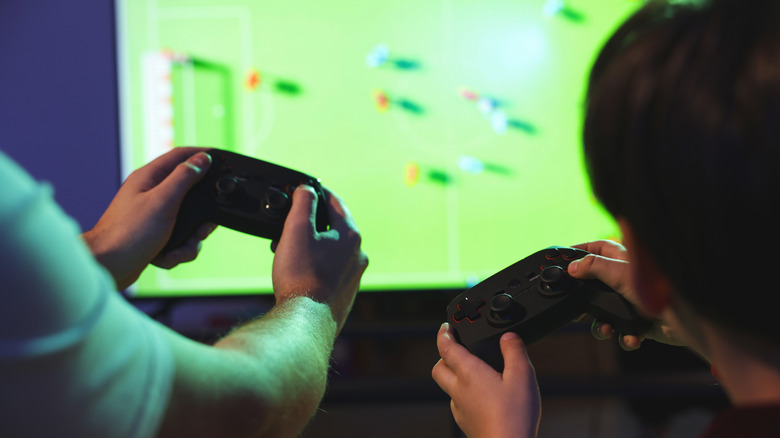 два человека играют в игру, используя игровые контроллеры перед телевизором