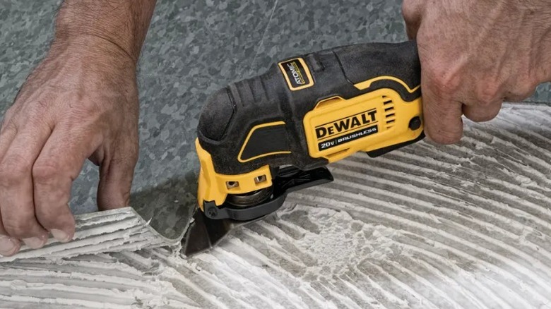 Человек, использующий многофункциональный инструмент DeWalt для удаления затирки пола.