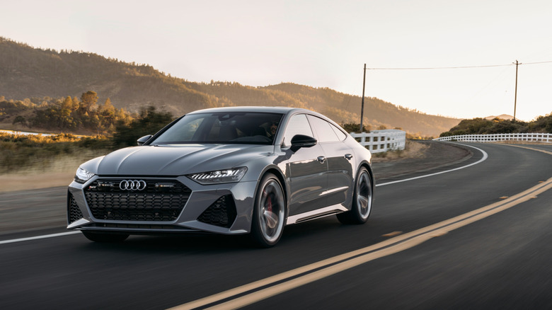 Вид спереди серого Audi RS7, едущего по сельской горной дороге.