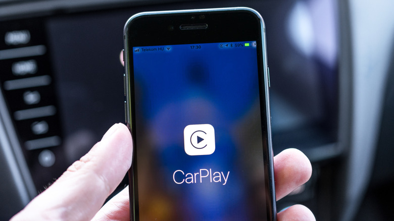 Человек держит в руках iPhone с отображенным на нем CarPlay.