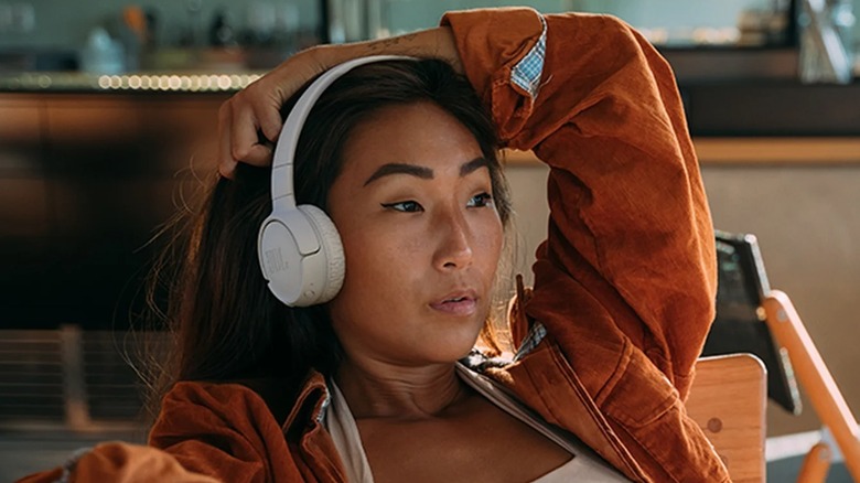 Женщина сидит в деревянном стуле и в наушниках JBL Tune 520BT