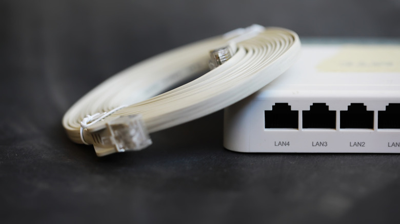 белый маршрутизатор с лежащим на нем кабелем Ethernet на черном фоне