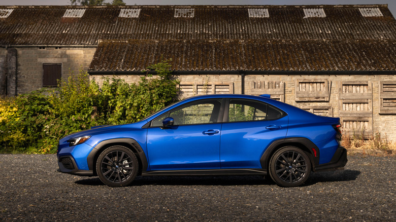 Вид сбоку на синий Subaru WRX 2026 года выпуска, припаркованный перед старым сараем.