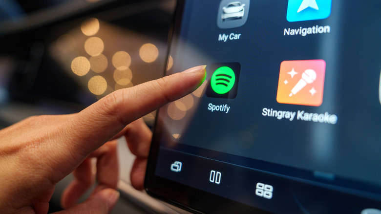 Палец крупным планом собирается нажать значок Spotify на экране автомобиля.