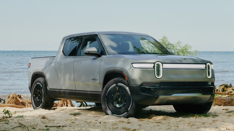 Серебристый Rivian R1T припаркован на песке возле воды