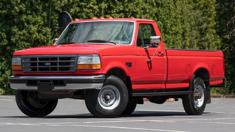 Красный пикап Ford с оригинальным 7,3-литровым двигателем Power Stroke на парковке, вид спереди в 3/4.