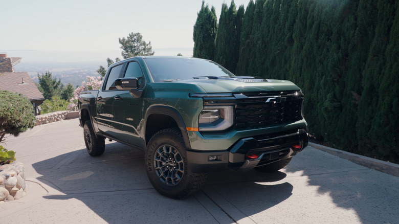 Chevrolet Silverado Trail Boss 2027 года в зеленом цвете на холмистой подъездной дороге, вид спереди в 3/4