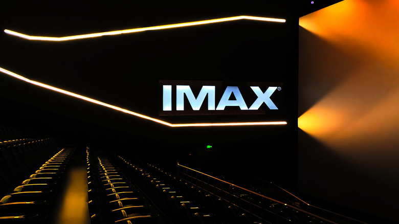 Внутри темного кинотеатра IMAX с освещенным логотипом IMAX на стене.