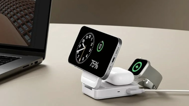 Белая беспроводная зарядная станция Anker, установленная рядом с ноутбуком и заряжающая телефон, наушники и часы