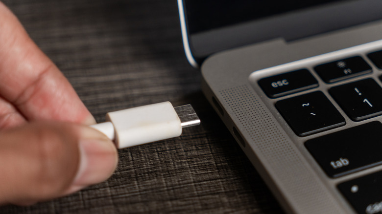 Крупный план руки, подключающей белый кабель USB-C к ноутбуку