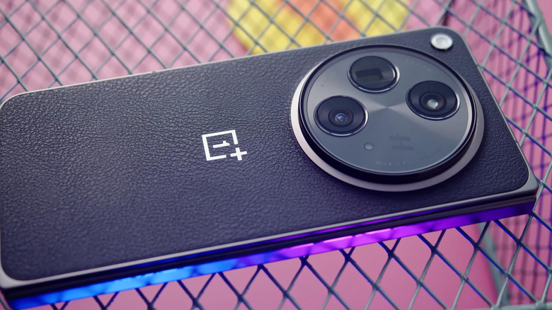Крупный план смартфона OnePlus 15, лежащего на проводной поверхности.