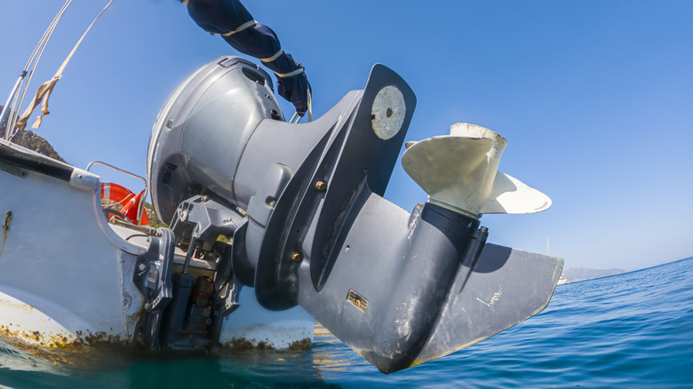 Серый подвесной лодочный мотор с поднятым пропеллером над морской водой